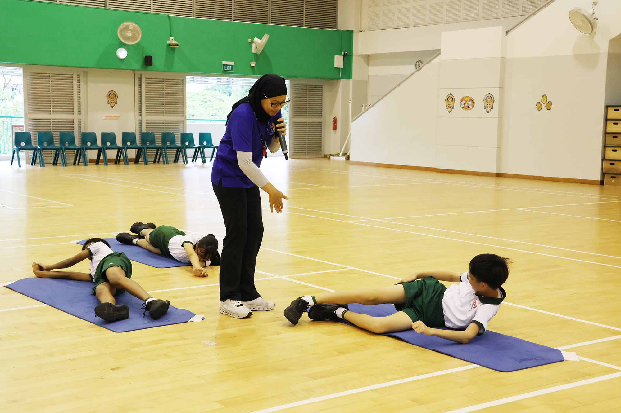 Students lie on exercise mats in the sports hall while an instructor demonstrates and guides them through a floor exercise during the I’m Possible sports engagement programme.
